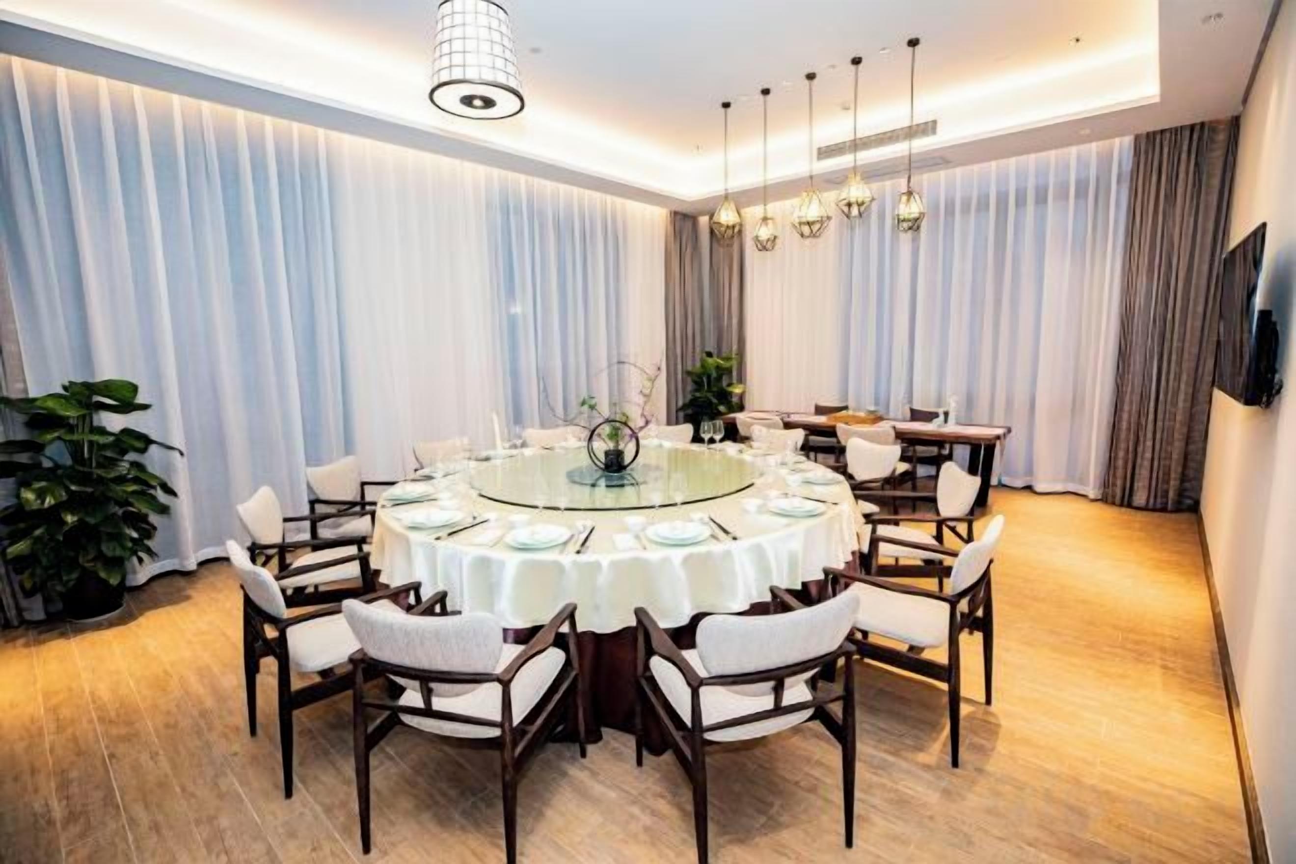Una mesa redonda con sillas, una araña y cortinas en una habitación con piso de madera.