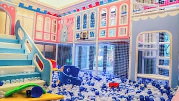 Un área de juegos interior con una piscina de pelotas, toboganes y una estructura para escalar.