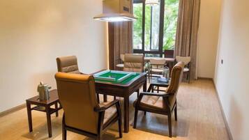 A room with a pool table, leather chairs, a sofa, and a window with curtains.
