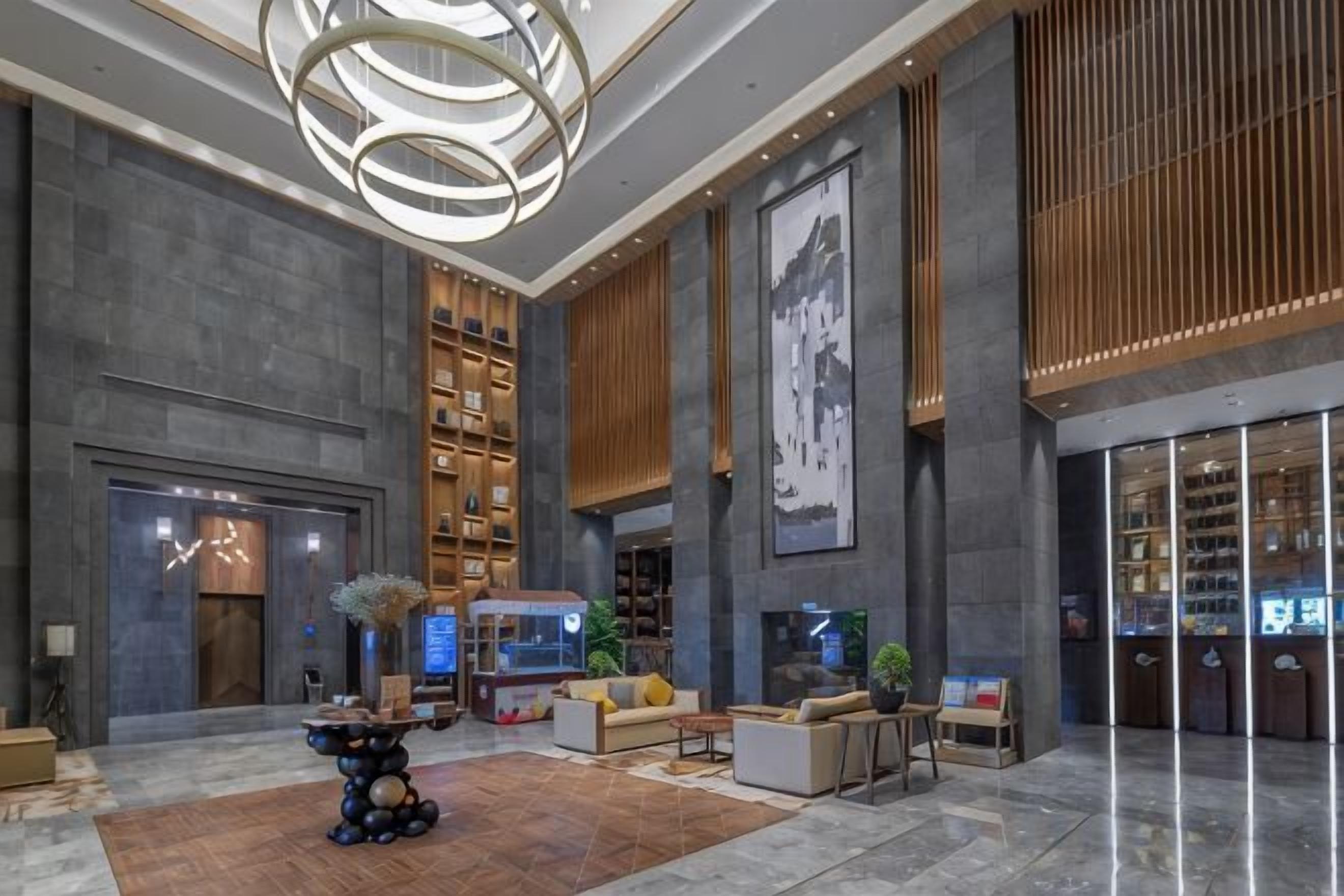 A spacious lobby with a central seating area, a large bookshelf, and a modern chandelier.