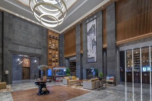 Un vestíbulo amplio con una zona de estar central, una gran estantería y un moderno candelabro.