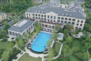 Un edificio grande con piscina, rodeado de vegetación y otros edificios residenciales.