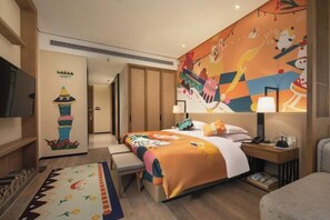 Une chambre d’hôtel avec un lit, une table de chevet, une lampe et une fresque murale colorée.