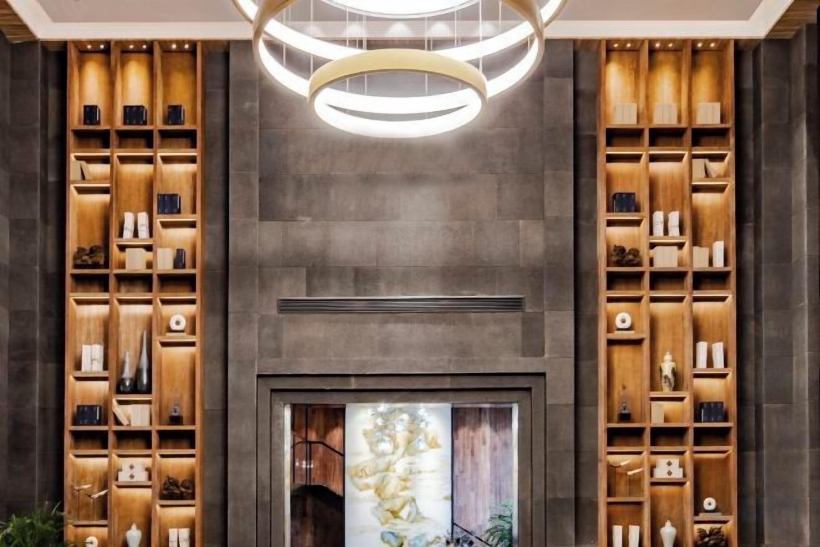 A modern interior with a central fireplace, wooden shelving units on either side, and a circular light fixture above.