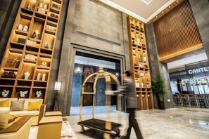 Un vestíbulo de hotel con una recepción, una amplia estantería de madera y una decoración de estilo moderno.