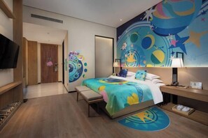 Et moderne hotelværelse med seng, sengebord, lampe og et farverigt mural på væggen.