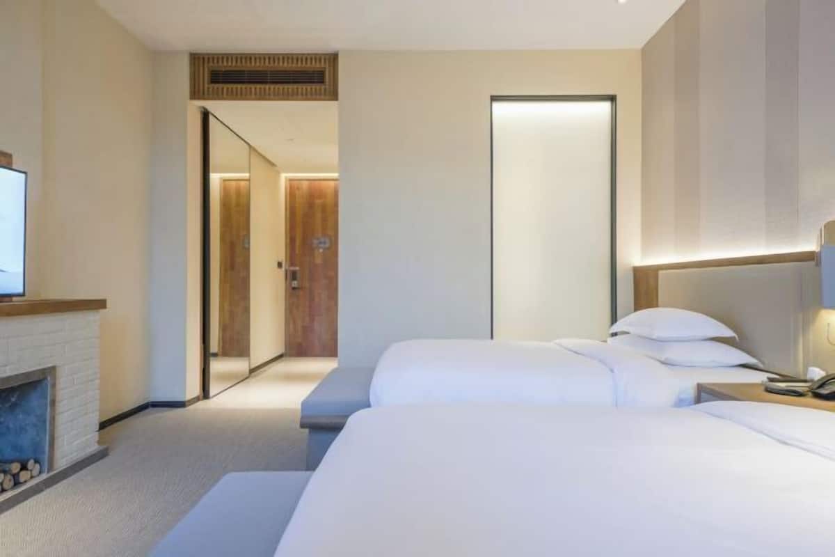 A hotel room with two beds, a fireplace, a mirror, and a door leading to another room.