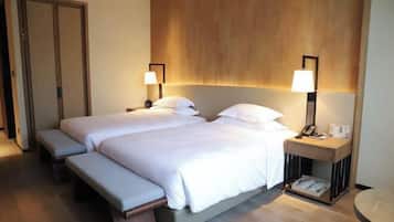 Una cama doble con una banca, mesitas de noche con lámparas y un cabecero de madera.