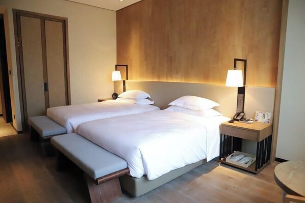 Una cama doble con una banca, mesitas de noche con lámparas y un cabecero de madera.