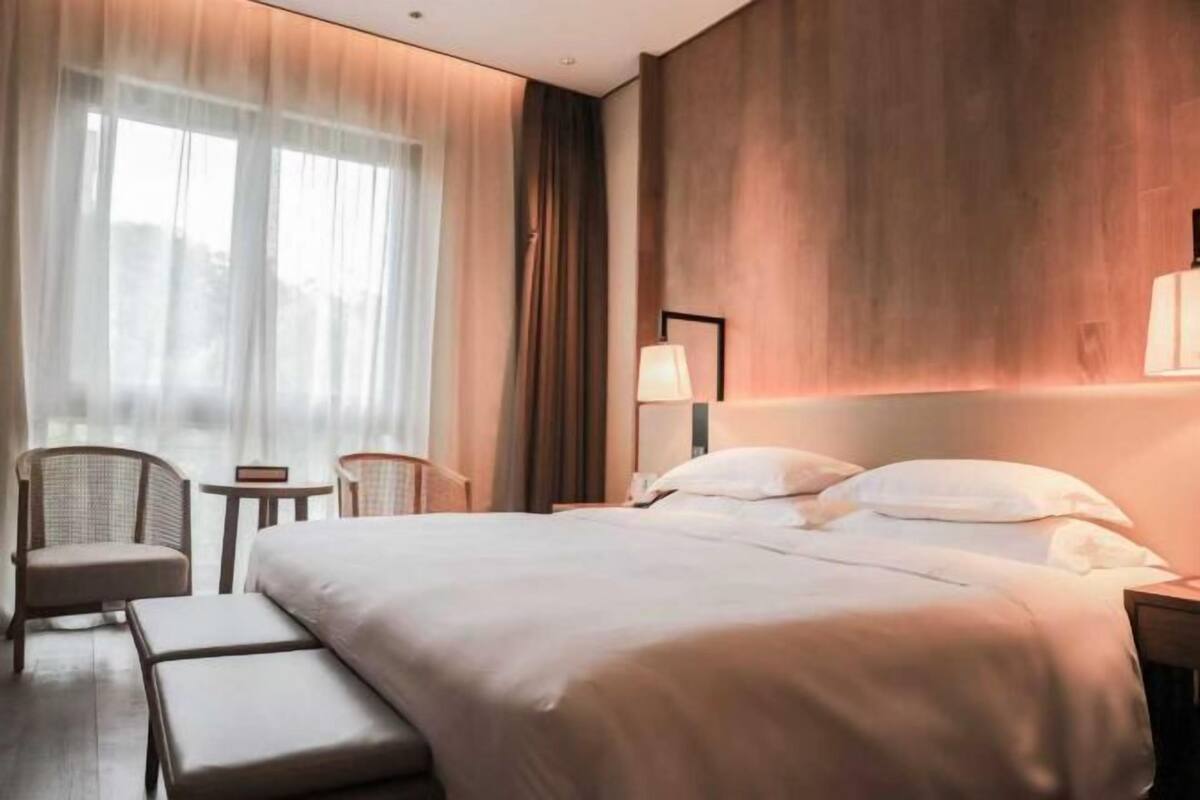 A hotel room with a large bed, a chair, a small table, and a lamp.