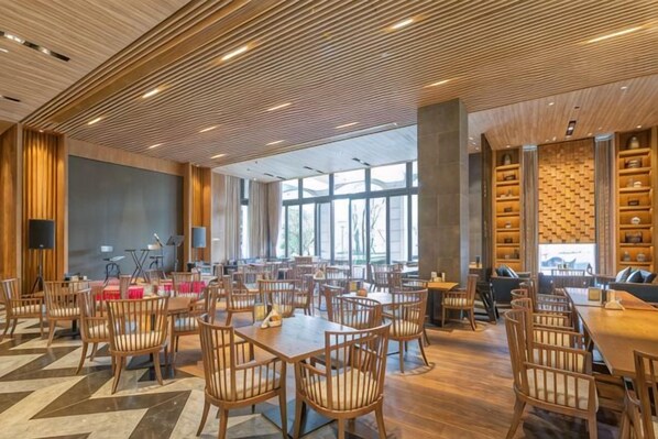 Un vaste espace dédié à la salle à manger, avec de nombreuses tables et chaises, de grandes fenêtres et un design moderne au niveau du plafond.