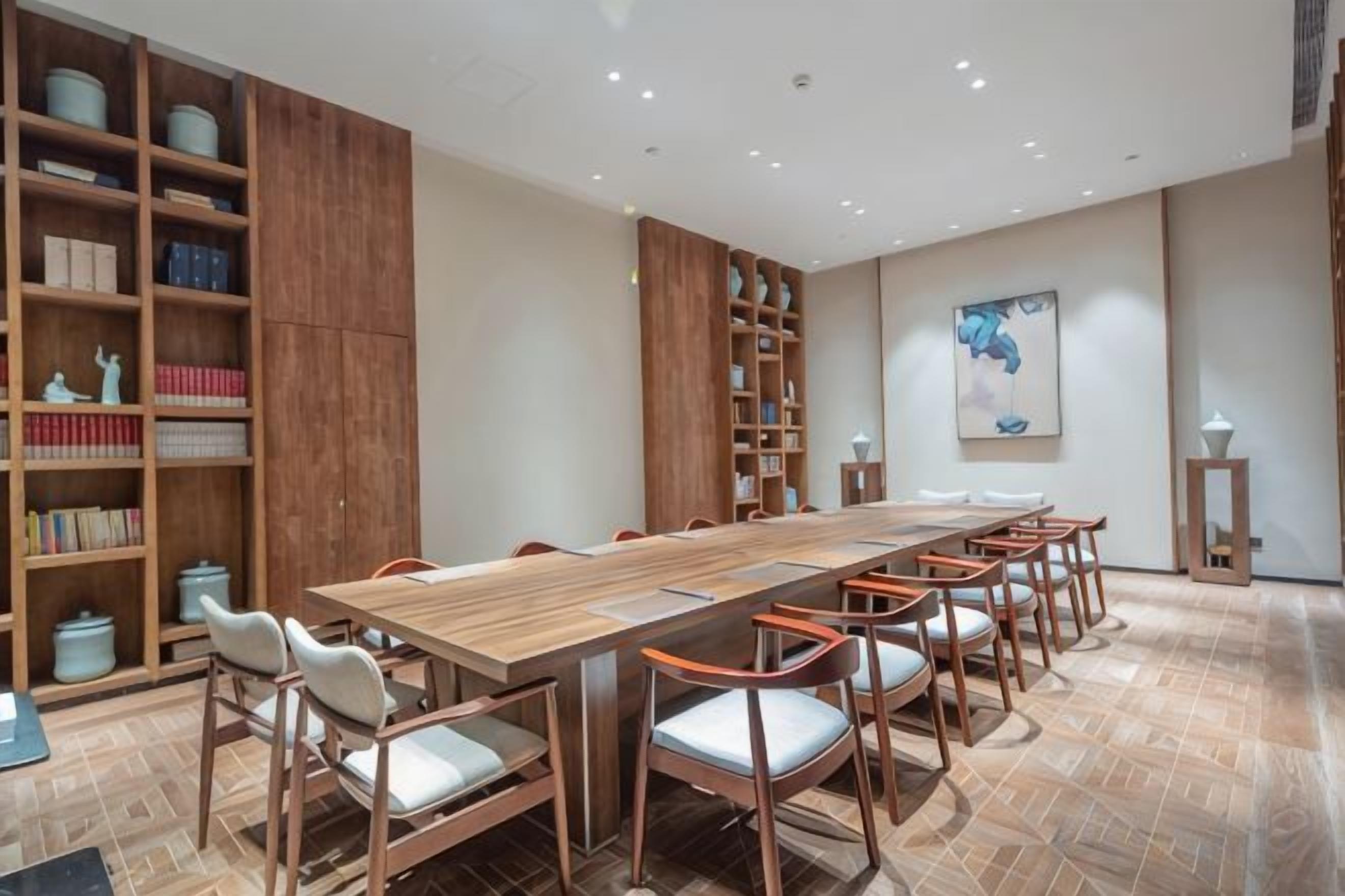 Un salón de conferencias con una larga mesa de madera, múltiples sillas y estanterías llenas de libros.