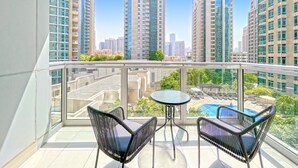 A balcony with two black wicker chairs and a small round table, overlooking a swimming pool and high-rise buildings. - bnbme | The Residences | 2 BDR (Dubai)