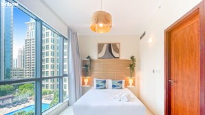 A modern hotel room with a large window, a bed with white linens, a wooden headboard, and a view of a swimming pool and high-rise buildings. - bnbme | The Residences | 2 BDR (Dubai)