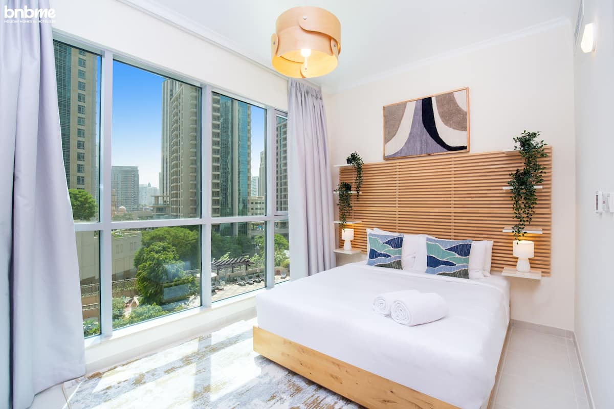 A modern bedroom with a large bed, a city view, and a wooden headboard.