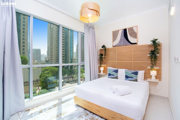 A modern bedroom with a large bed, a city view, and a wooden headboard.