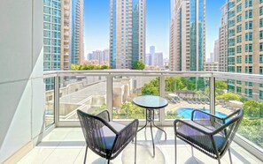 Ein Balkon mit zwei schwarzen Korbstühlen und einem kleinen runden Tisch, mit Blick auf einen Swimmingpool und hohe Gebäude.