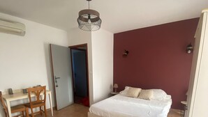 Un dormitorio con cama, un escritorio y una silla, una puerta y una lámpara fijada a la pared.