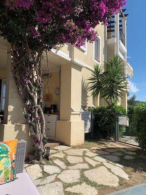 A two-story building with a stone patio, a tree with purple flowers, and a palm tree.