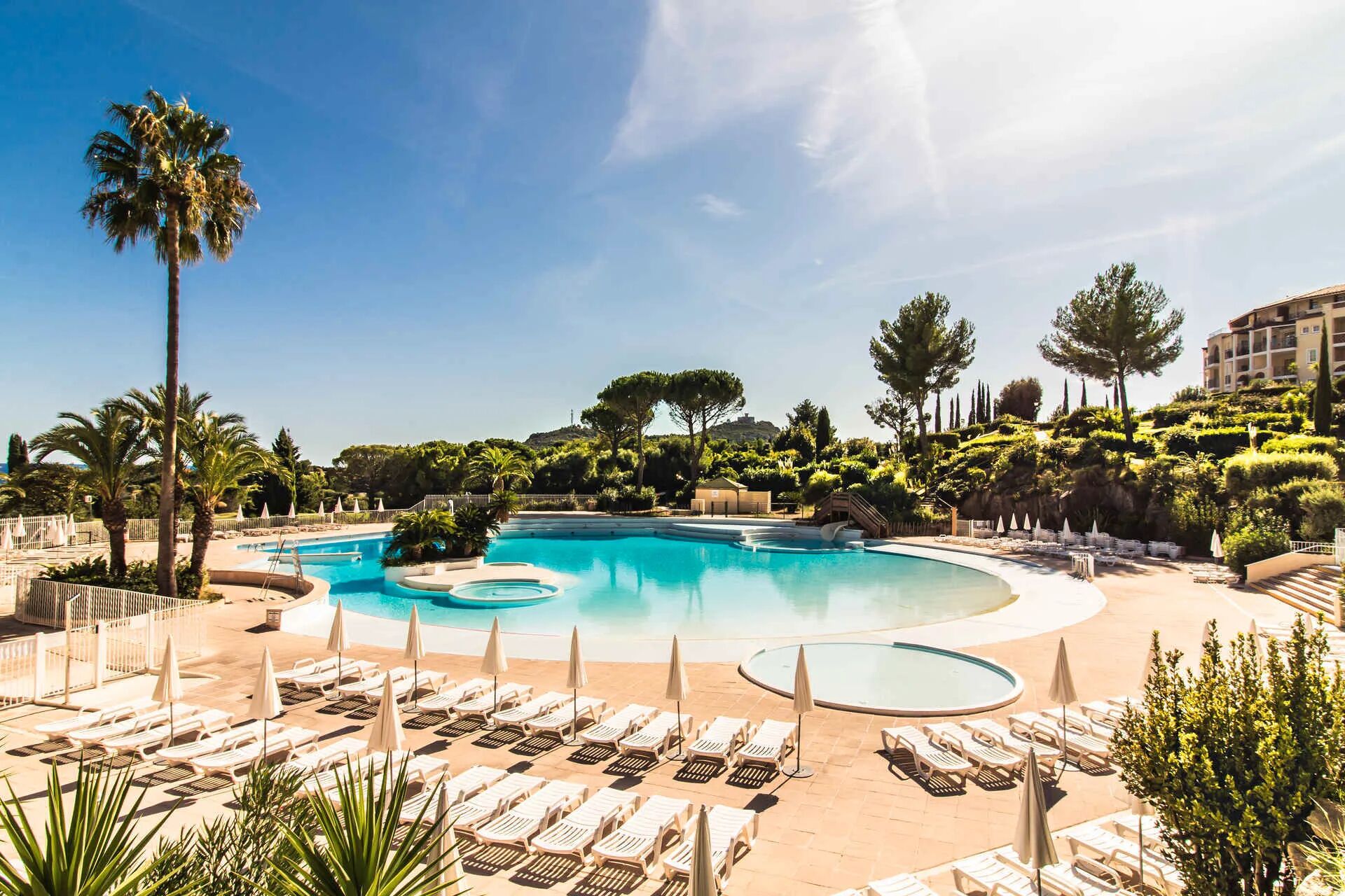A resort pool area with multiple swimming pools, sun loungers, and palm trees.