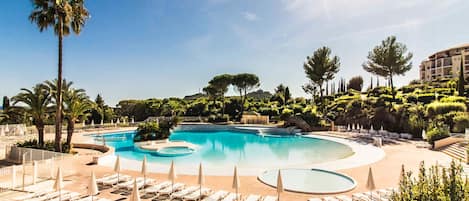 A resort pool area with multiple swimming pools, sun loungers, and palm trees.