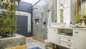Ein modernes Badezimmer mit Dusche aus Beton, einem weißen Waschtisch und hängenden Pflanzen.