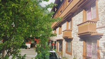 Um edifício tradicional com varandas de madeira e paredes de pedra, um caminho de paralelepípedos e um carro estacionado.