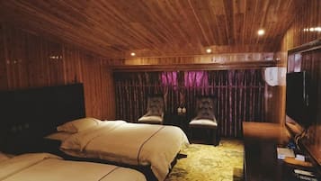 Quarto com painéis de madeira, duas camas, televisão e um espaço de estar com cadeiras.