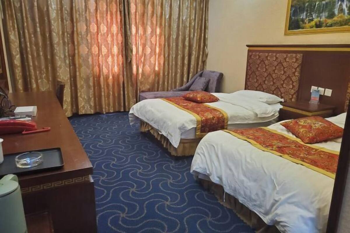 A hotel room with two beds, a desk, a chair, and a small table.