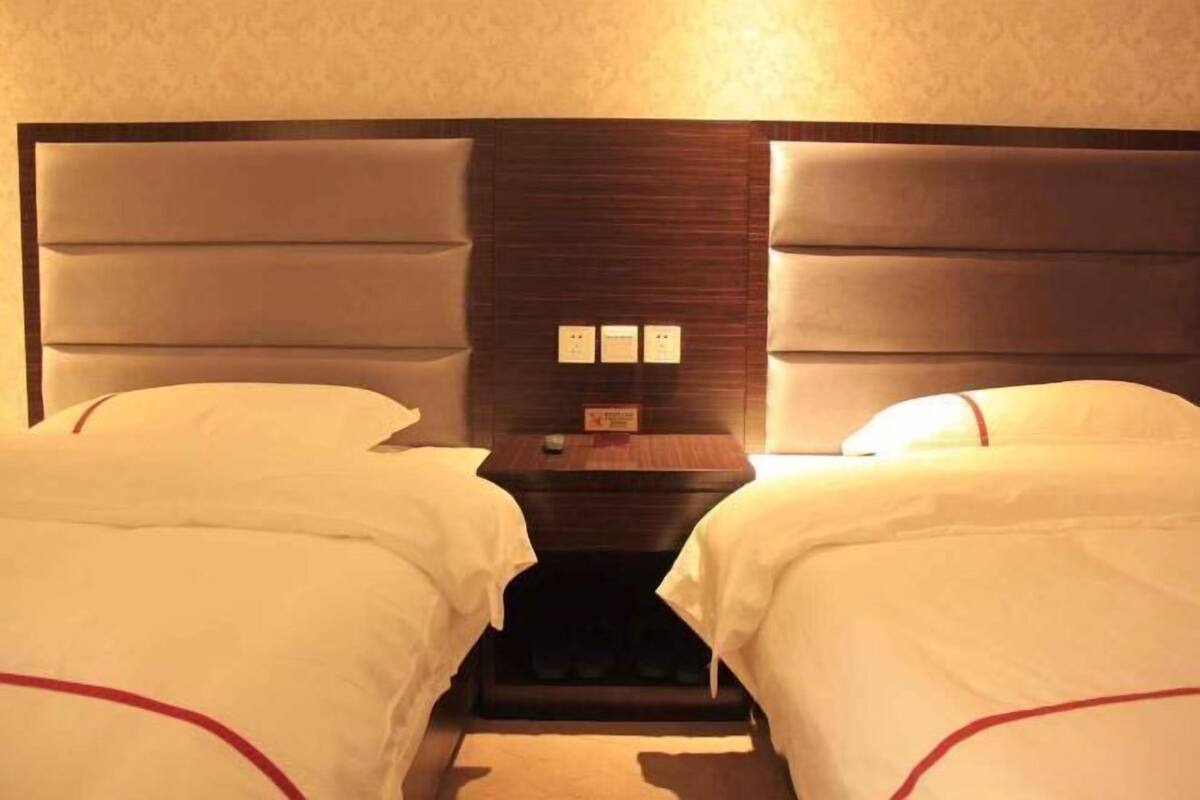 A hotel room with two beds, a wooden headboard, and a nightstand with a clock and a small table.