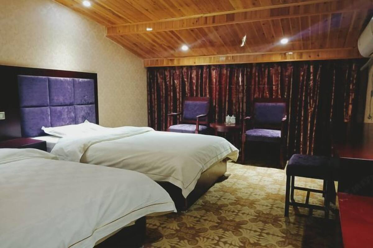 A hotel room with two beds, a wooden ceiling, and a patterned carpet.