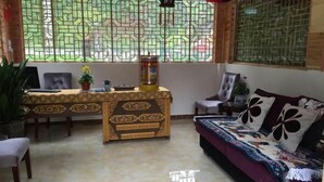Una sala de estar con un sofá, una mesa de centro y un televisor. Se ve una ventana con un panel decorativo y vistas a áreas verdes al exterior.