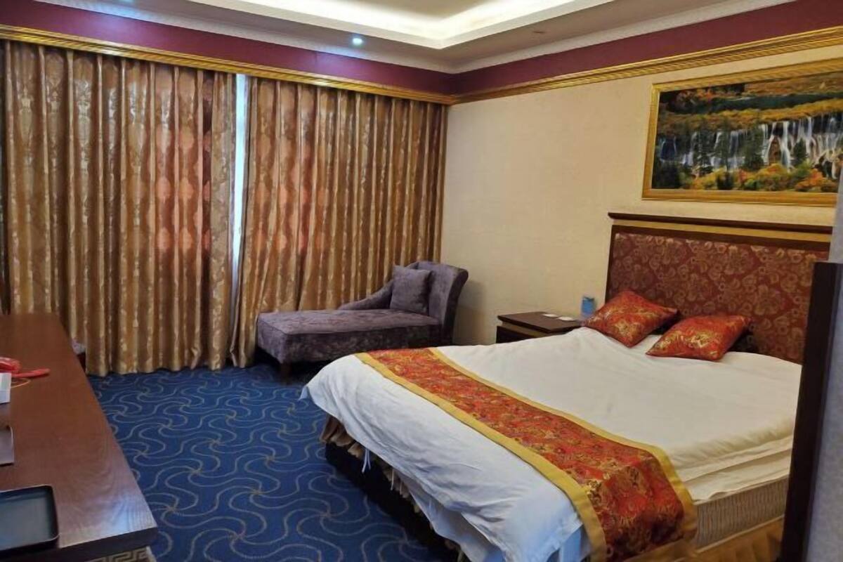 A hotel room with a bed, a desk, a chair, a nightstand, and a painting on the wall.