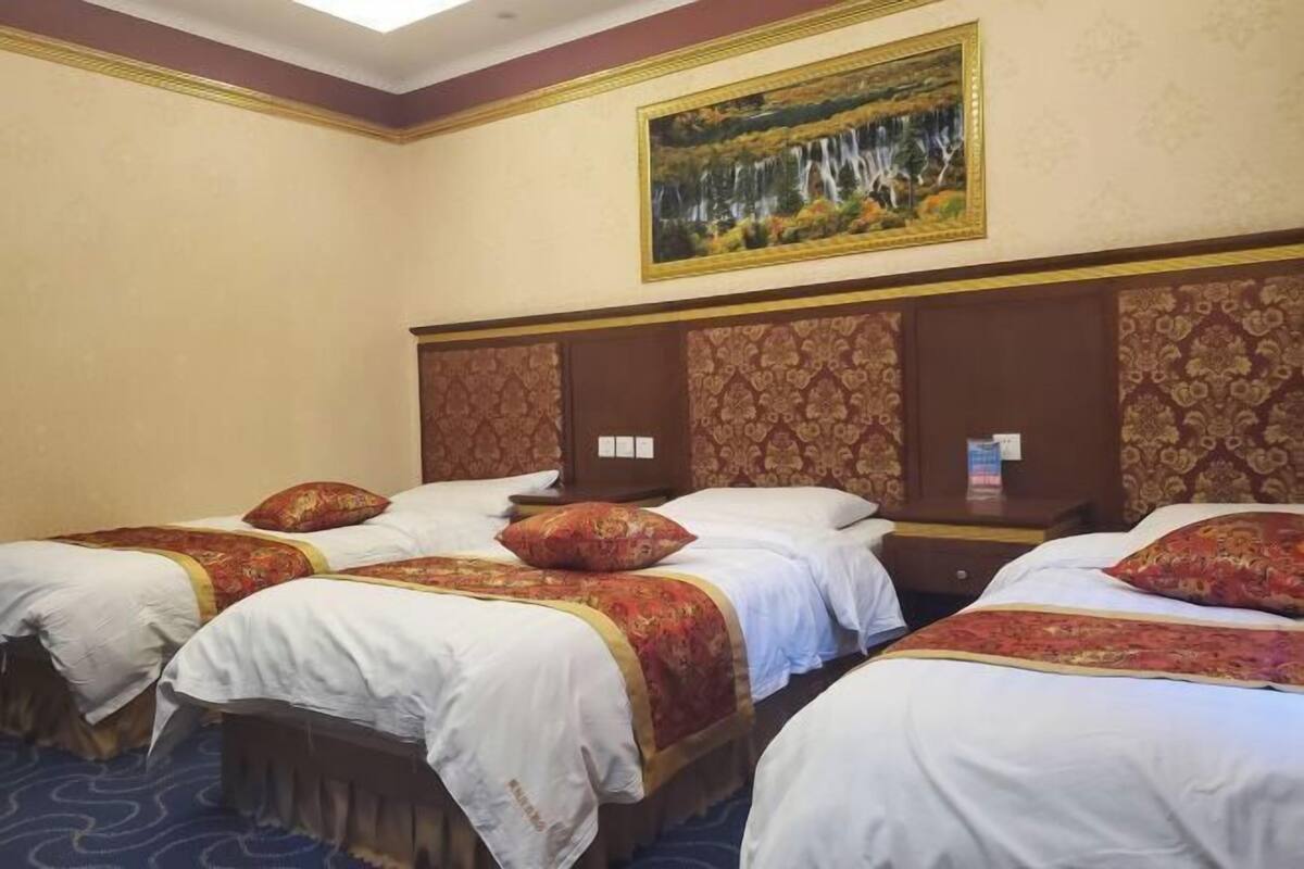 A hotel room with four beds, a painting of a waterfall, and a patterned wall.