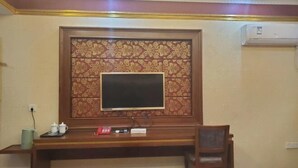 Habitación de hotel con un escritorio de madera, televisor, toma de corriente y aire acondicionado de pared.