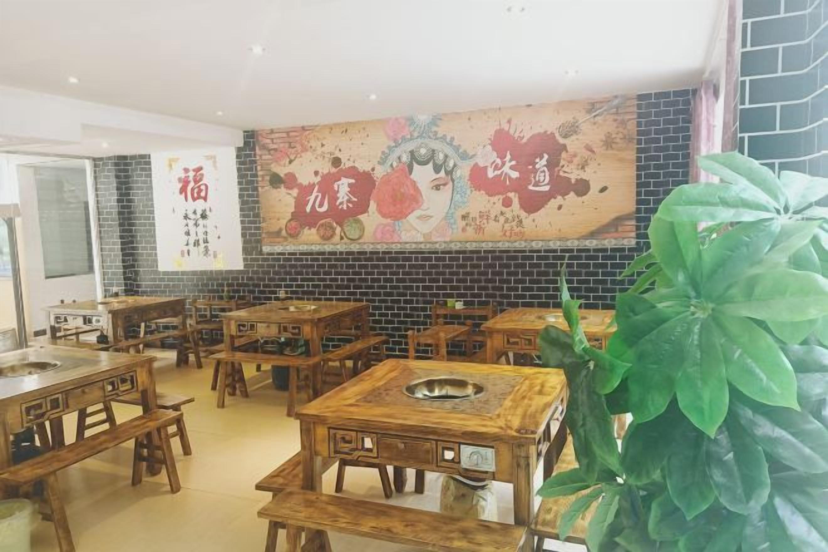 L’intérieur d’un restaurant avec des tables et des chaises en bois, un grand mur décoratif et une plante en pot.