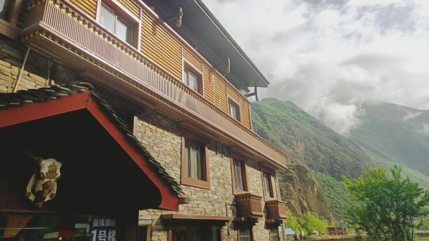 Un edificio tradicional con balcón, paredes de piedra y montañas al fondo.