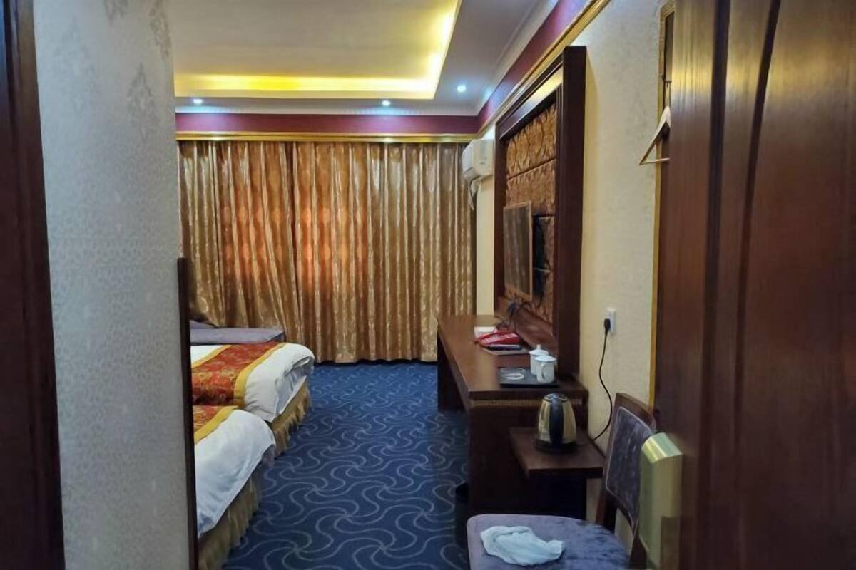A hotel room with two beds, a desk with a chair, a television, and a window with curtains.