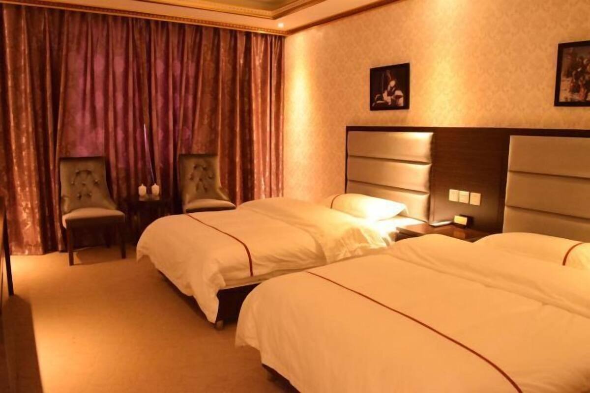 A hotel room with two beds, a nightstand, a chair, and a large window with curtains.