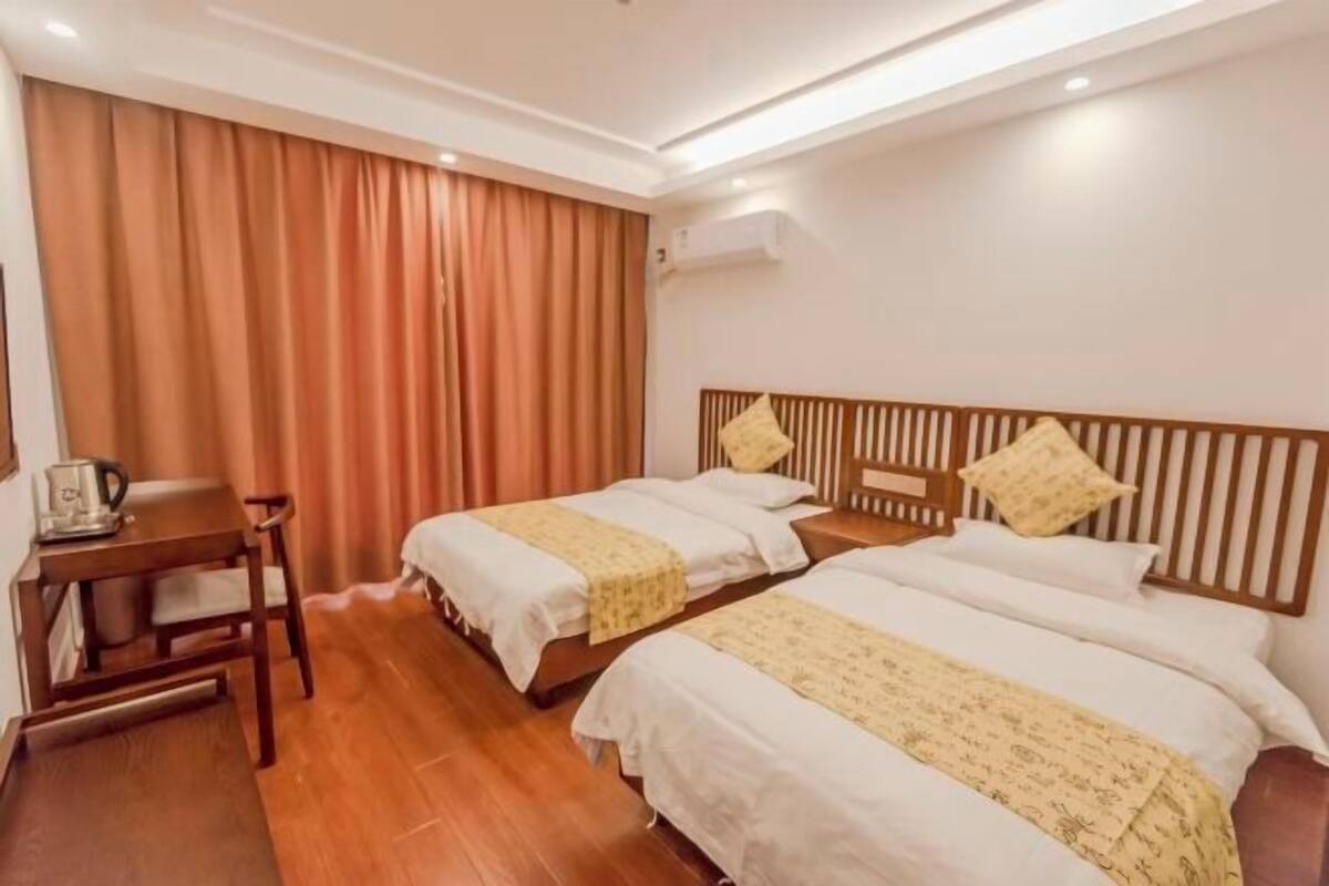 Hotellihuone, jossa on kaksi sänkyä, puinen työpöytä, tuoli ja ilmastointilaite.