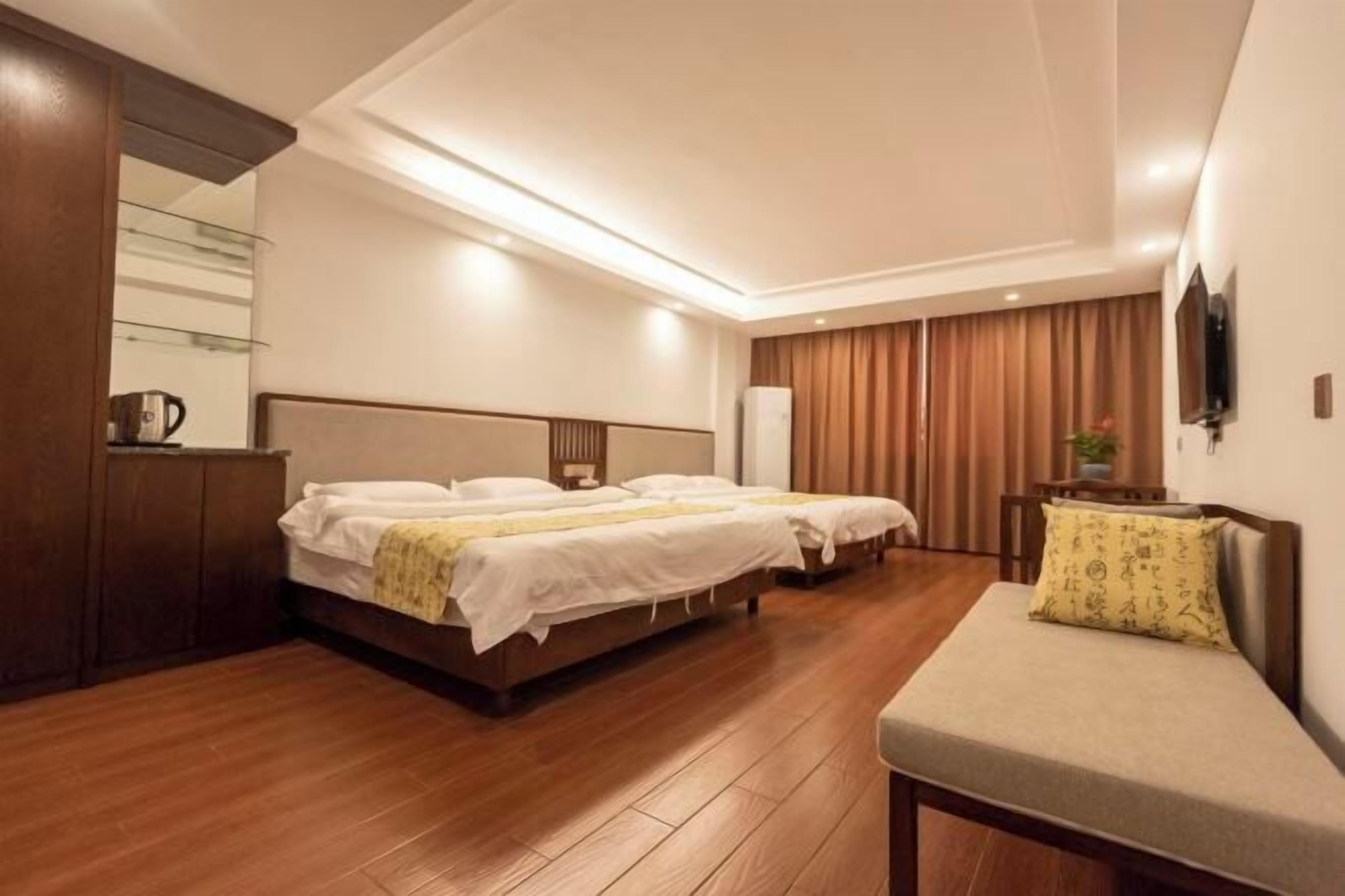 A hotel room with two beds, a wooden floor, a sofa, a TV, and a wardrobe.