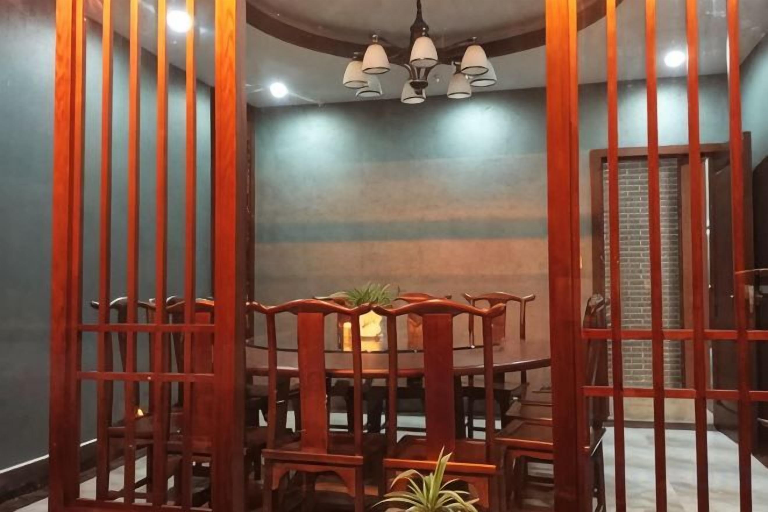 A dining area with a wooden table and chairs, a chandelier, and a brick wall in the background.