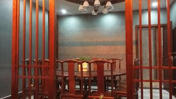 A dining area with a wooden table and chairs, a chandelier, and a brick wall in the background.