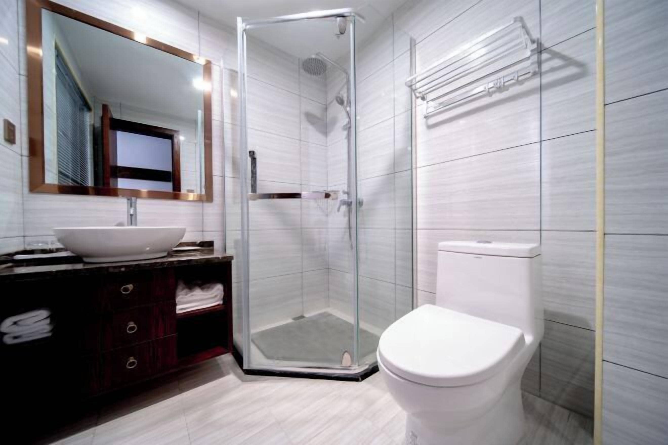 A modern bathroom with a glass-enclosed shower, a white toilet, and a vanity with a large mirror and a vessel sink.