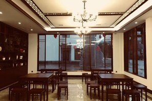 A dining area with multiple tables and chairs, a chandelier, and large windows with a view. - Wuyuan Qingyun Hotel (Wuyuan)