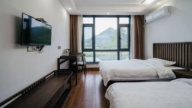 Une chambre d’hôtel avec deux lits, un téléviseur fixé au mur, un bureau et une grande fenêtre donnant sur la montagne.