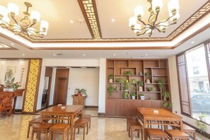 Un hall d’hôtel avec des meubles en bois, un lustre et des étagères ornées de plantes.