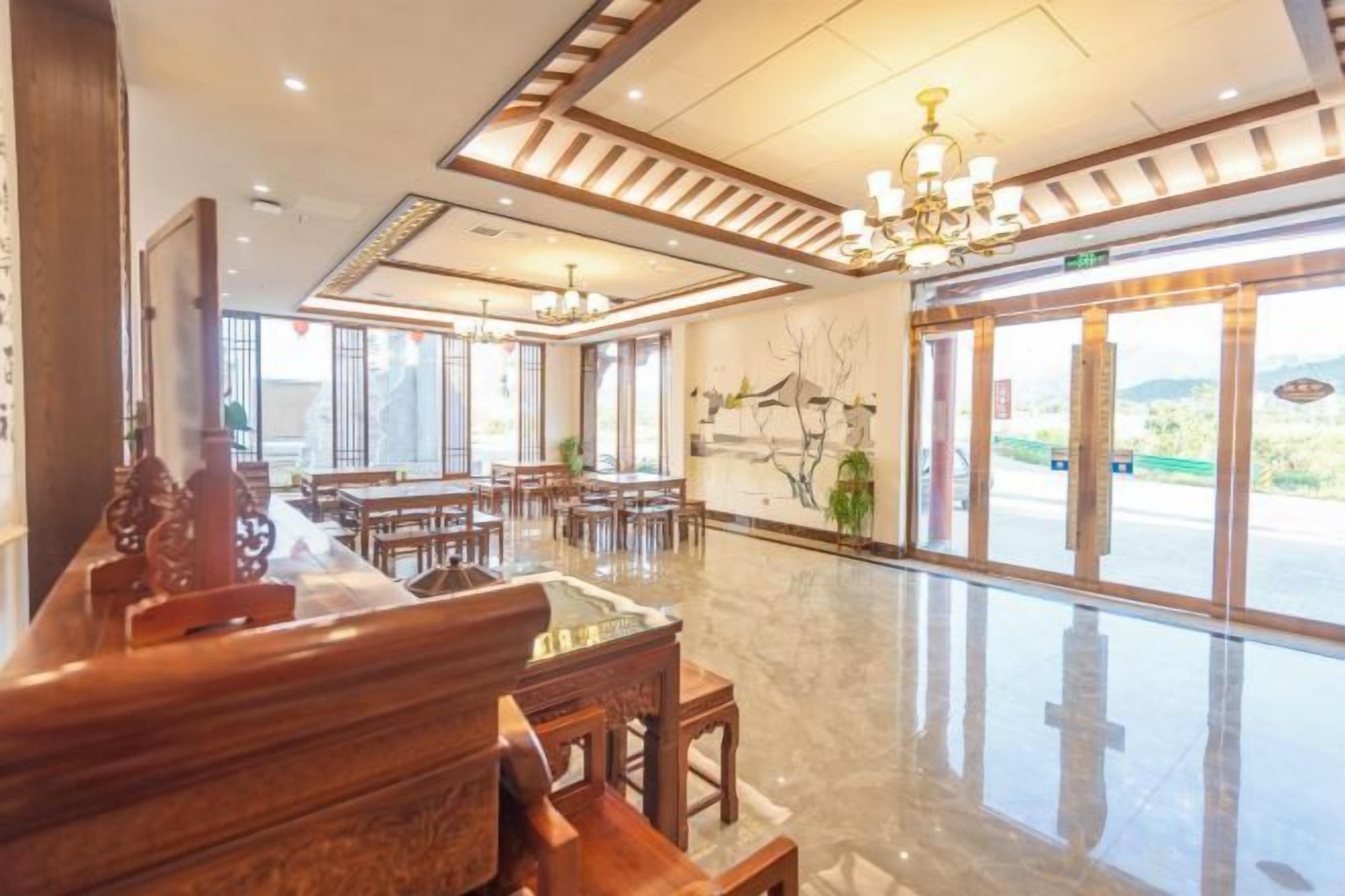 A spacious hotel lobby with wooden furniture, a chandelier, and large windows offering a view of the outdoors.