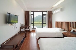 Ein Hotelzimmer mit zwei Betten, einem Fernseher, einem Schreibtisch und einem großen Fenster mit Blick auf die Berge.