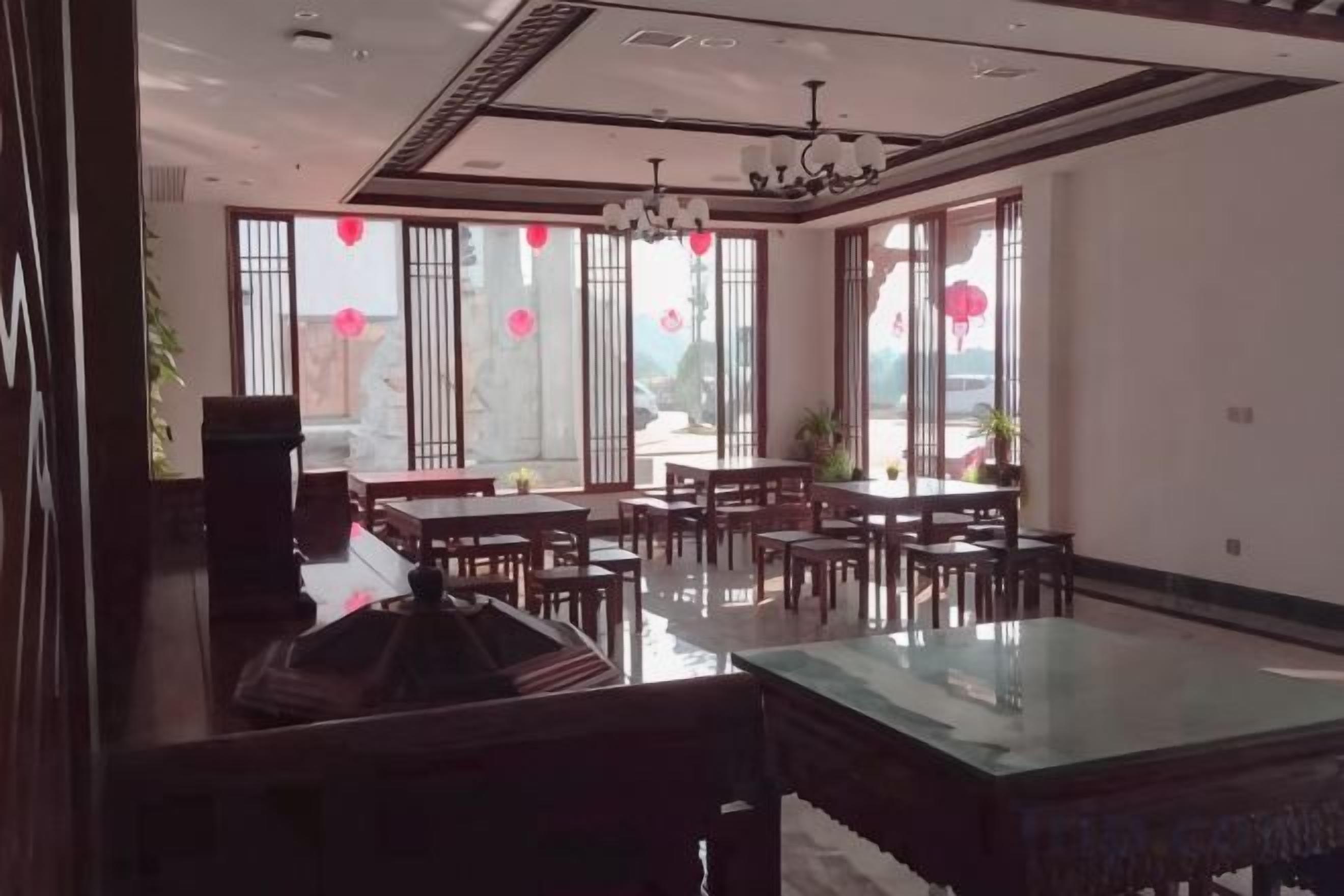 A spacious dining area with multiple tables and chairs, large windows with red decorations, and a modern ceiling design.